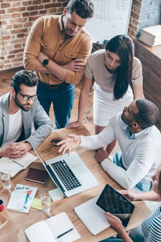 Top view part of group of five young people discuss something and gesturing while leaning to the table in office